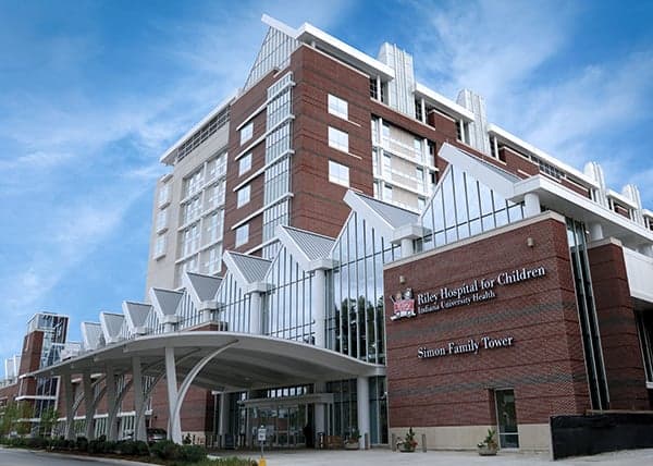 Riley Hospital for Children building under a blue sky, featuring a sign with the Riley wagon logo and hospital name.