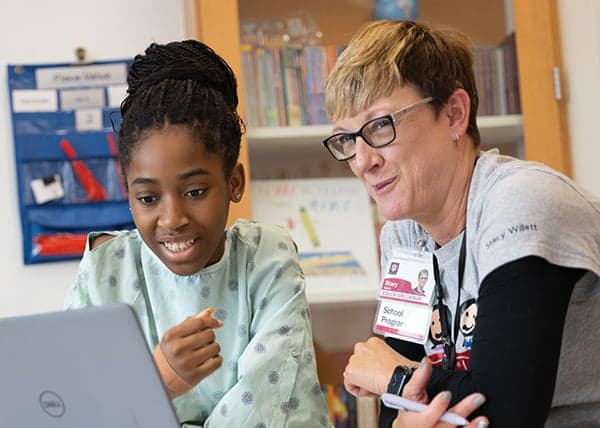 Riley patient working on a school lesson on a computer with a Riley School Program Education Liaison